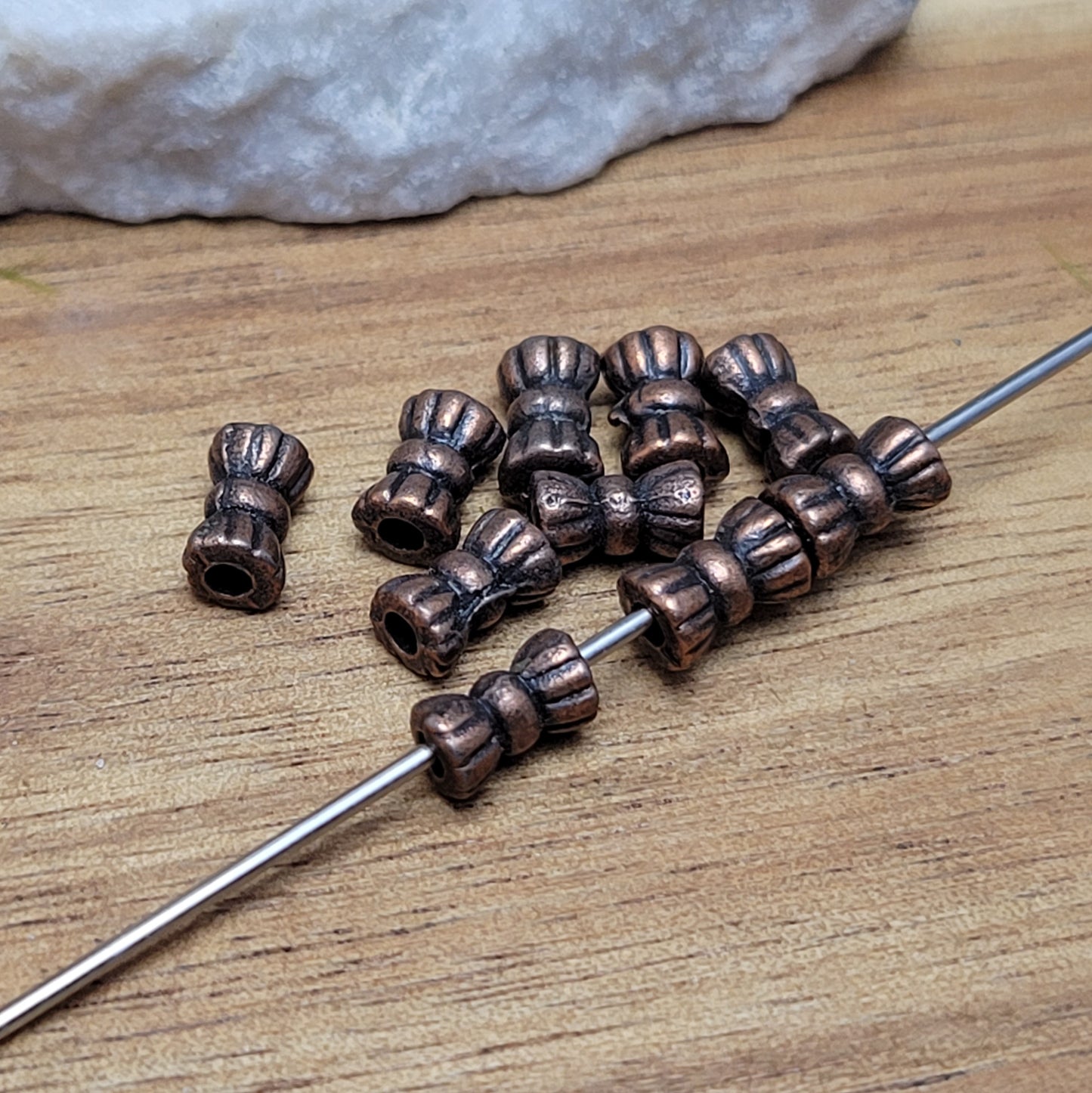 Diese Packung enthält 10 kleine Metallperlen in antik kupferfarbig. Die Perlen haben die Form eines kleinen aufgeplusterten Schleifchens. Das Fädelloch der Perlen verläuft durch den langen Teil der Perle.