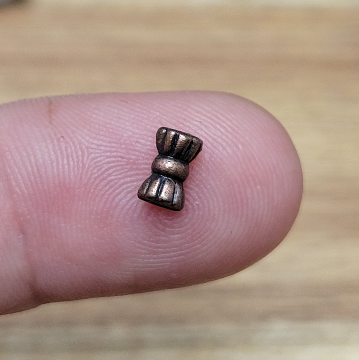 Diese Packung enthält 10 kleine Metallperlen in antik kupferfarbig. Die Perlen haben die Form eines kleinen aufgeplusterten Schleifchens. Das Fädelloch der Perlen verläuft durch den langen Teil der Perle.