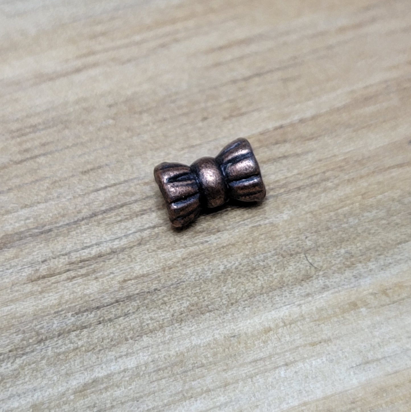 Diese Packung enthält 10 kleine Metallperlen in antik kupferfarbig. Die Perlen haben die Form eines kleinen aufgeplusterten Schleifchens. Das Fädelloch der Perlen verläuft durch den langen Teil der Perle.