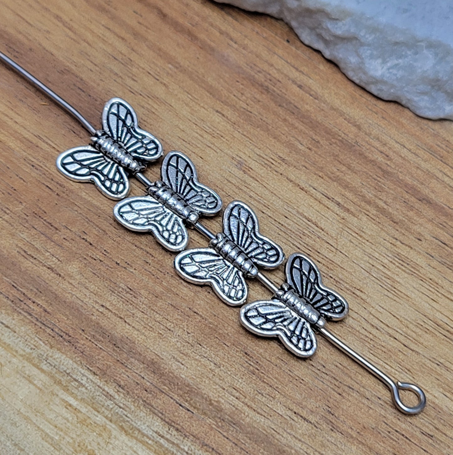 Eine Packung mit 5 Metallperlen in Form eines Schmetterlings. Die Perlen sind beidseitig geprägt, antik silberfarbig und haben eine hübsches Antikfinish, was für einen tollen Vintage-Effekt sorgt. Das Fädelloch verläuft von oben nach unten durch den Schmetterling.