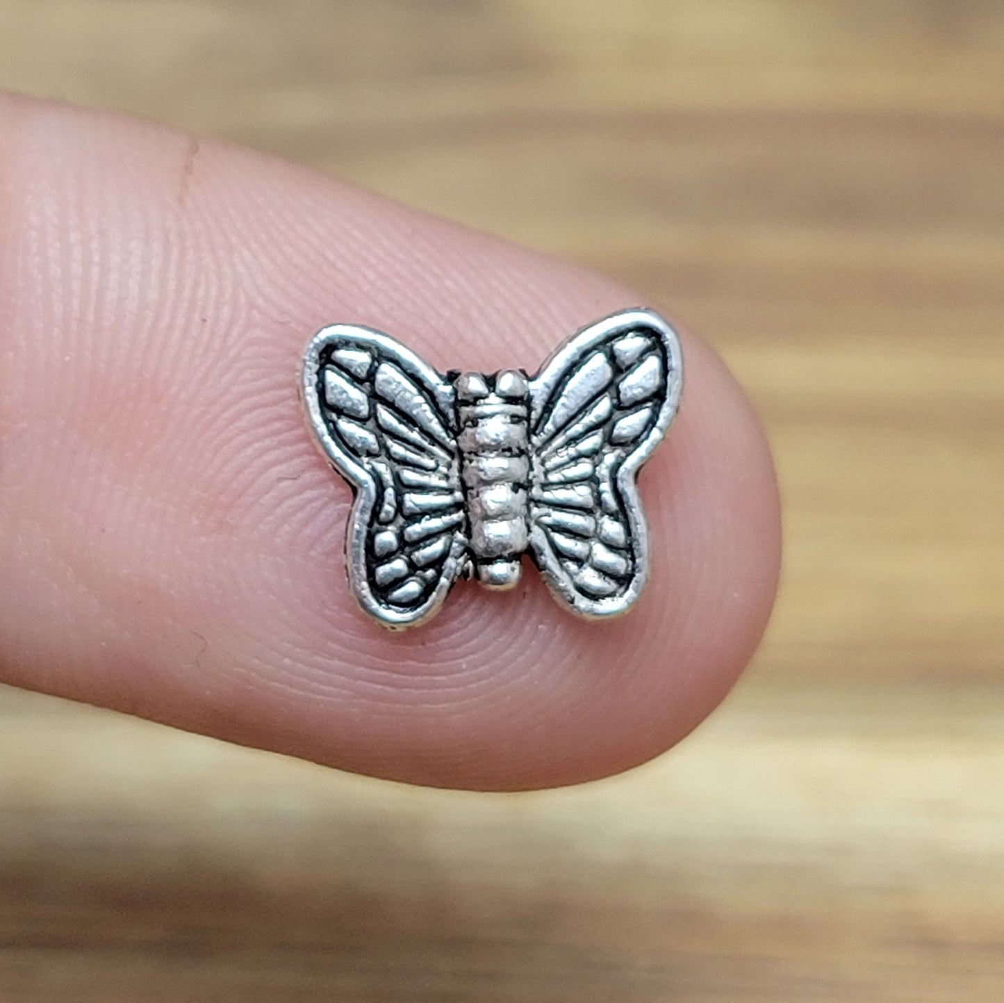 Eine Packung mit 5 Metallperlen in Form eines Schmetterlings. Die Perlen sind beidseitig geprägt, antik silberfarbig und haben eine hübsches Antikfinish, was für einen tollen Vintage-Effekt sorgt. Das Fädelloch verläuft von oben nach unten durch den Schmetterling.