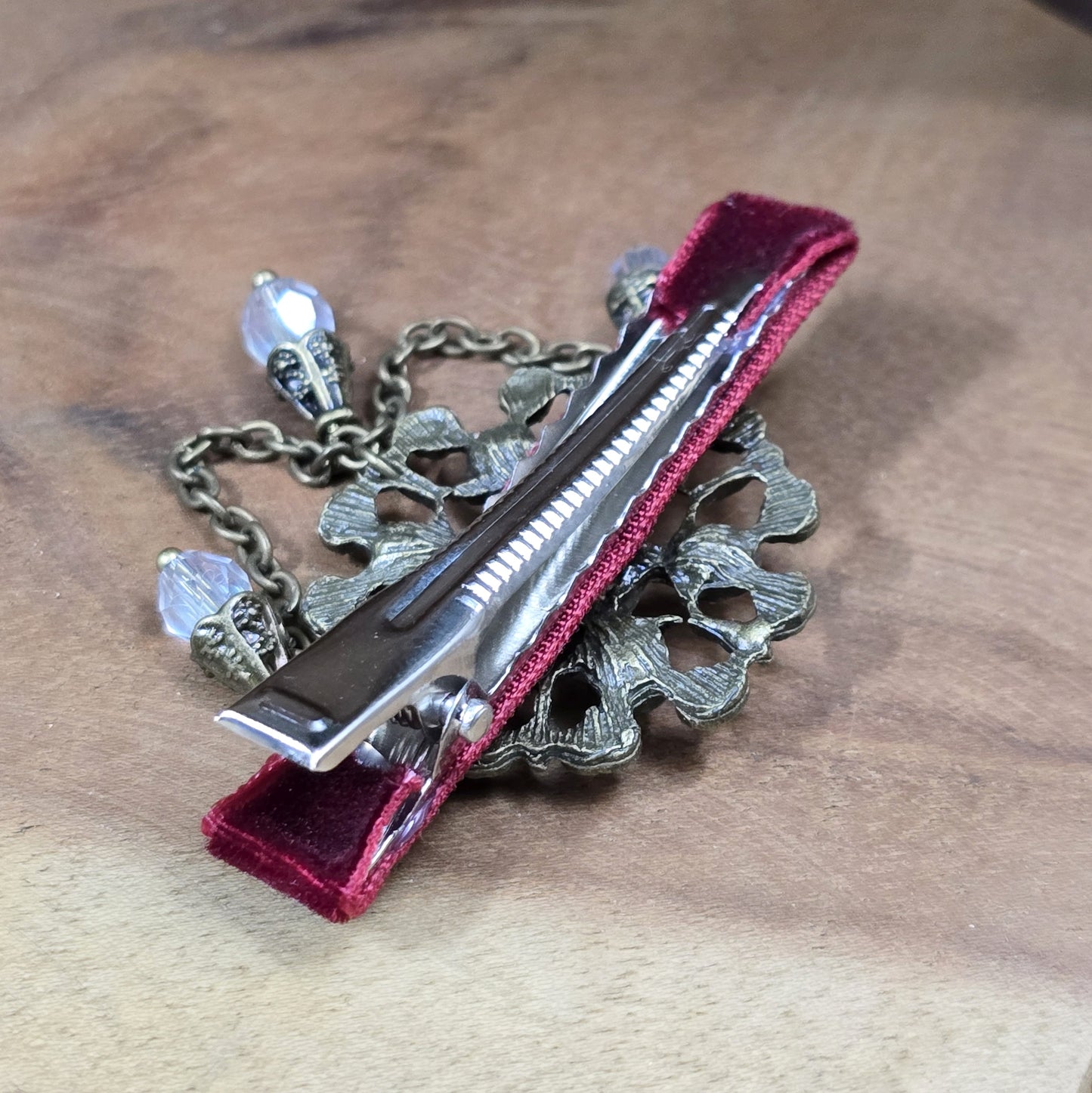 Das Bild zeigt eine Krokodilspange im Vintagelook mit Strass und dunkelrotem Samt, Kristallglasanhänger, Kettchen, Einzelstück
Lass dich von der zeitlosen Eleganz vergangener Epochen verzaubern mit dieser exquisiten Krokodilspange im Vintagestil. Sie ist kunstvoll verziert mit einem filigranen, antik bronzefarbigen Schmuckteil, welches mit funkelndem Strass besetzt ist.