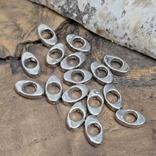 16 schöne ovale Metallperlen in Antiksilber, Augenform, 10mm. Die Perlen haben einen runden Ausschnitt in der Mitte und ein längs verlaufendes Fädelloch. Sie eignen sich hervorragend als Abstandhalter oder für dezente Akzente in Armbändern, Ketten und Ohrschmuck. Menge: 16 Stück.