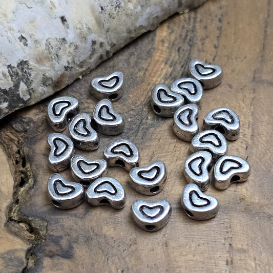 20 kleine Metallperlen in Herzform, antiksilberfarben, mit feinen Intarsien. Größe: 5 x 7 mm. Ideal für Schmuckprojekte wie Armbänder und Ketten. Das Fädelloch verläuft längs und erleichtert das Auffädeln auf verschiedene Drähte. Menge: 20 Stück.