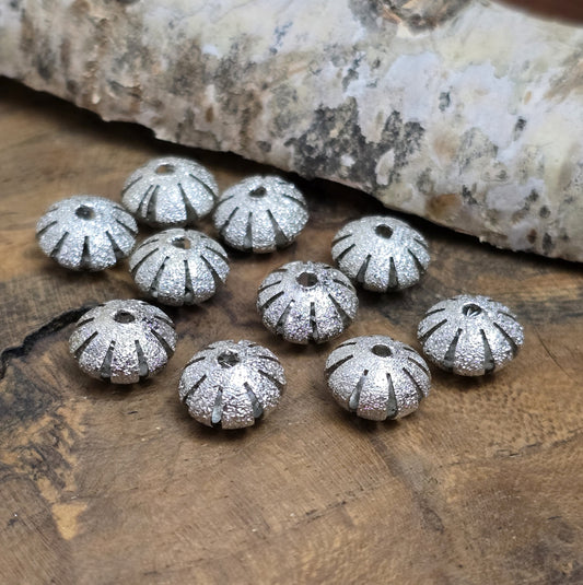 10 silberfarbene Stardust-Metallperlen, 10 x 6 mm, in UFO-Form mit glitzernder Oberfläche und gefächertem Rand. Ideal für Schmuckprojekte wie Armbänder, Ketten oder Ohrringe. Fädelloch: 1,6 mm. Perfekt für edle und stilvolle Akzente.