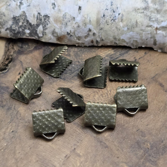 Bandklemme mit Zähnen, antik bronzefarbig, 8 mm breit. Ideal zum Befestigen von Verschlüssen an Stoffbändern. Einfach mit einer Zange am Bandende fixieren – für sicheren Halt und eine dekorative Optik.