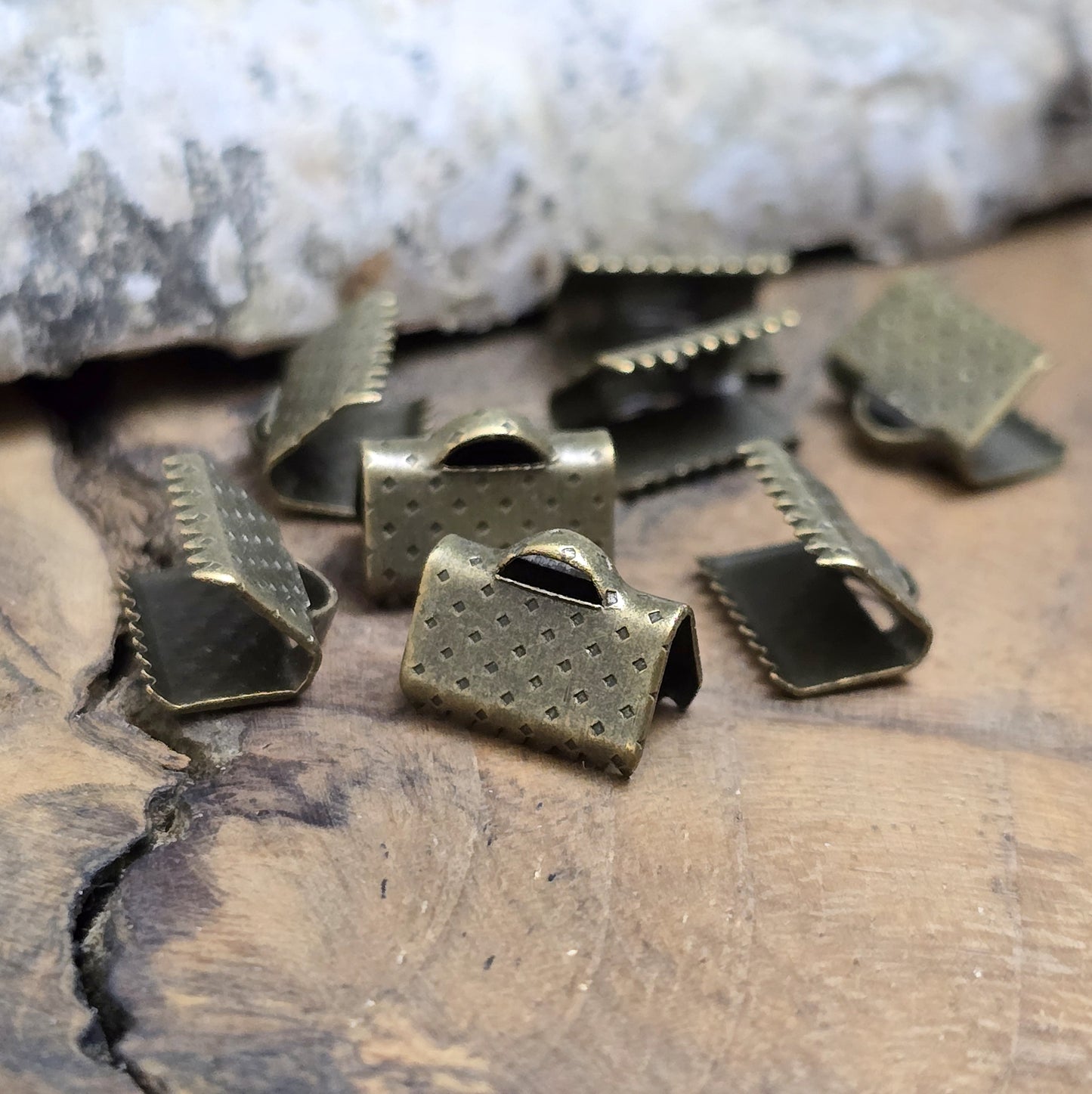 Das Bild zeigt antik bronzefarbige Bandklemmen mit Zähnen, 10 mm breit – ideal zum Befestigen von Verschlüssen an Stoffbändern. Einfach mit einer Zange auf das Bandende klemmen.