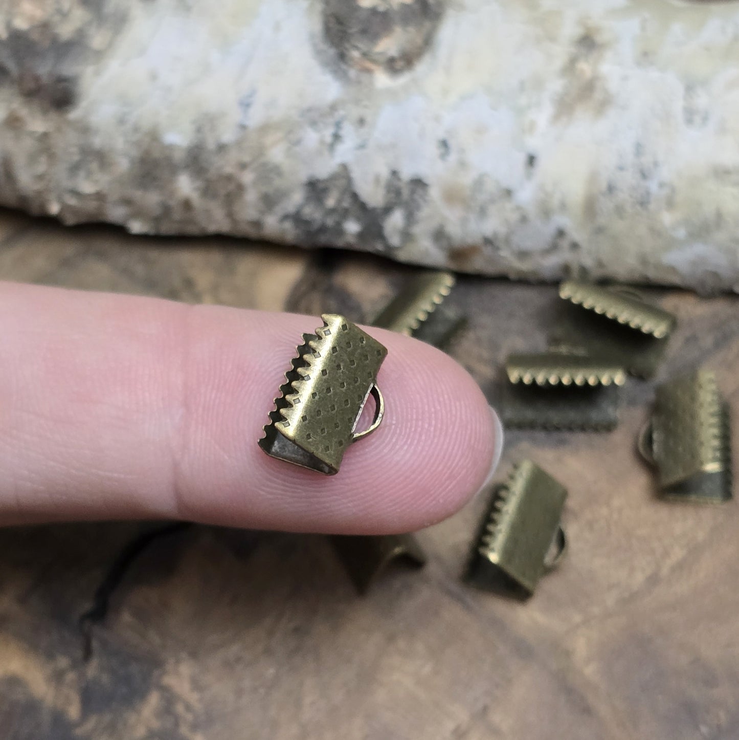 Das Bild zeigt antik bronzefarbige Bandklemmen mit Zähnen, 10 mm breit – ideal zum Befestigen von Verschlüssen an Stoffbändern. Einfach mit einer Zange auf das Bandende klemmen.