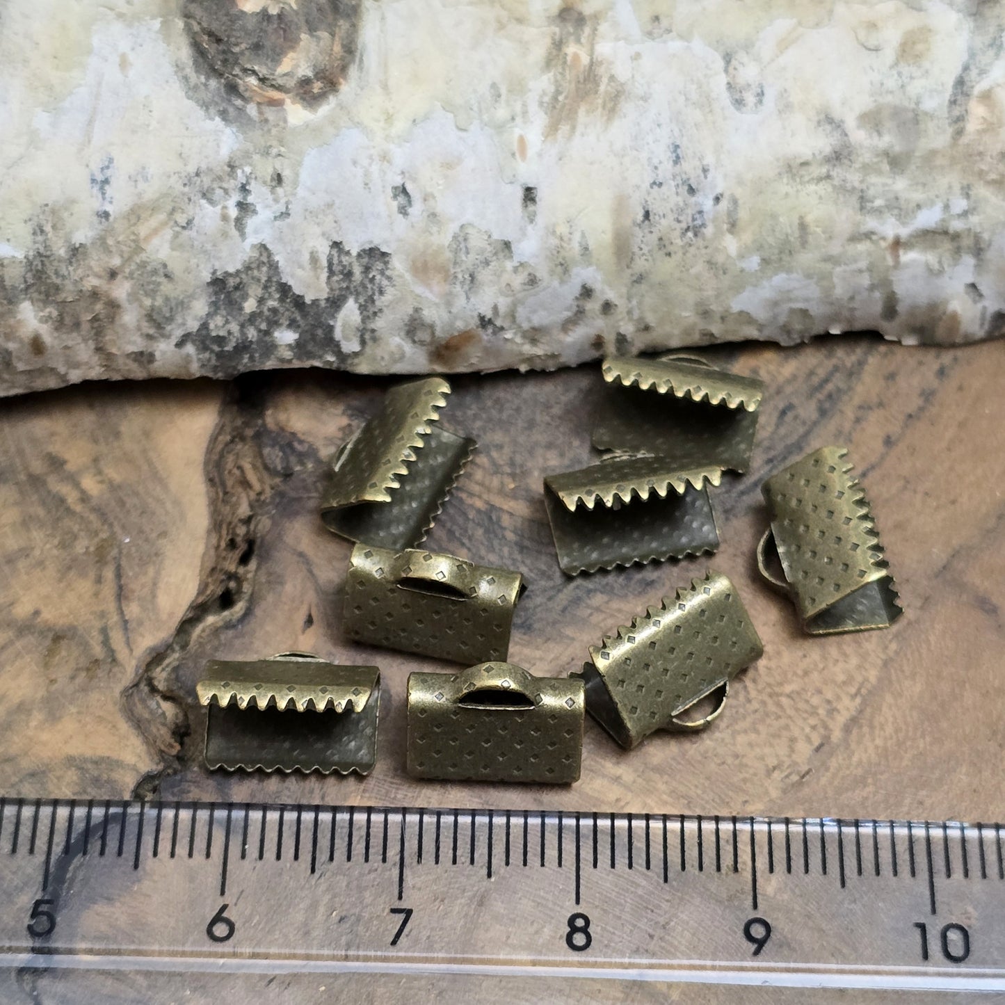 Das Bild zeigt antik bronzefarbige Bandklemmen mit Zähnen, 10 mm breit – ideal zum Befestigen von Verschlüssen an Stoffbändern. Einfach mit einer Zange auf das Bandende klemmen.