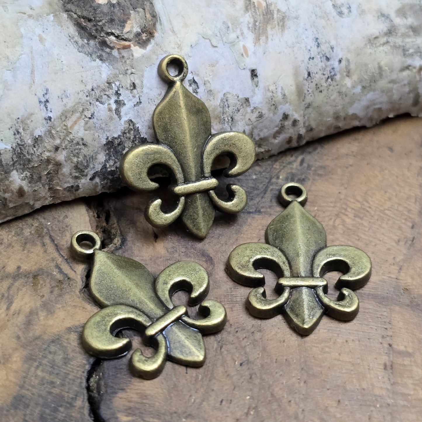 Das Bild zeigt 3 Anhänger Fleur de Lys 22mm, antik bronzefarbig. Ideal für die individuelle Schmuckfertigung.