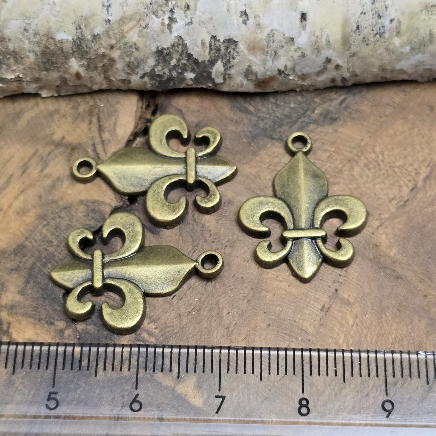 Das Bild zeigt 3 Anhänger Fleur de Lys 22mm, antik bronzefarbig. Ideal für die individuelle Schmuckfertigung.