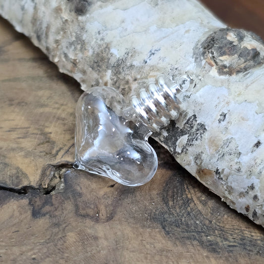 Kleiner Phiolenanhänger aus Glas, in Form eines Herzens mit silberfarbiger Kappe. Ideal zum Befüllen mit beschriftetem Reiskorn, Sand, Milchzahn, Asche, Haare udg.