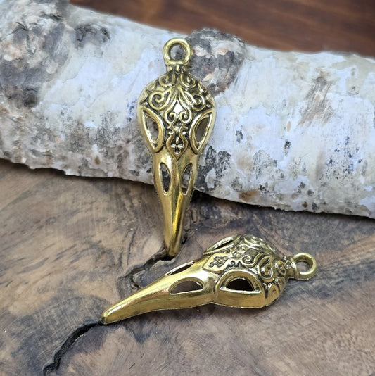 Das Bild zeigt einen detaillierten Krähenschädel mit Intarsien, gehalten in antik goldfarbenem Finish. Er ist einseitig geprägt und hat eine hohle Rückseite, was ihn leicht und vielseitig macht.