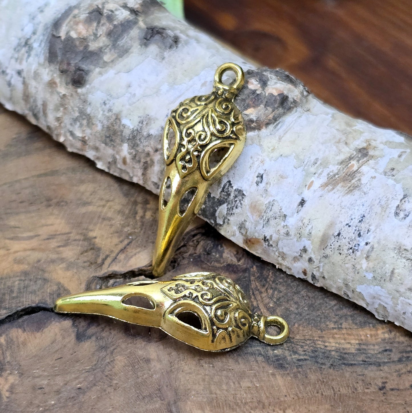 Das Bild zeigt einen detaillierten Krähenschädel mit Intarsien, gehalten in antik goldfarbenem Finish. Er ist einseitig geprägt und hat eine hohle Rückseite, was ihn leicht und vielseitig macht.