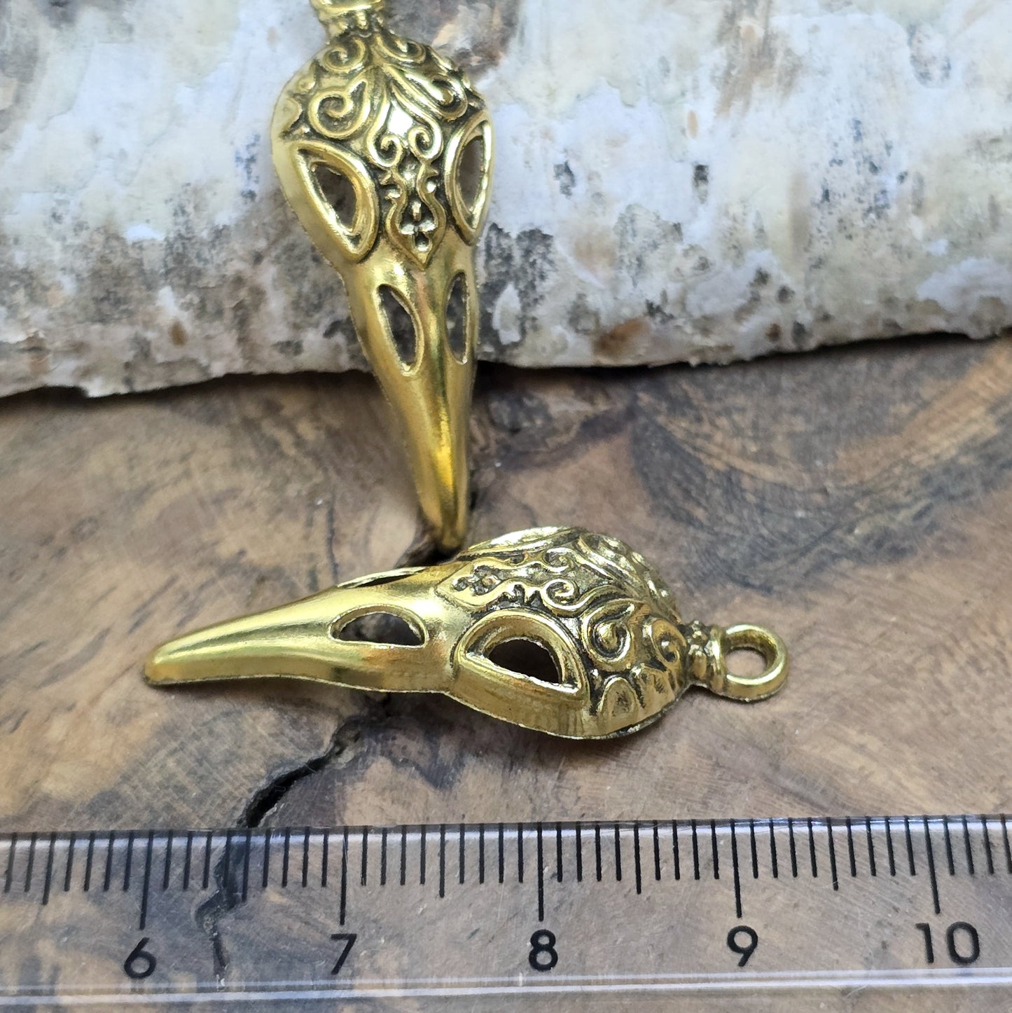 Das Bild zeigt einen detaillierten Krähenschädel mit Intarsien, gehalten in antik goldfarbenem Finish. Er ist einseitig geprägt und hat eine hohle Rückseite, was ihn leicht und vielseitig macht.