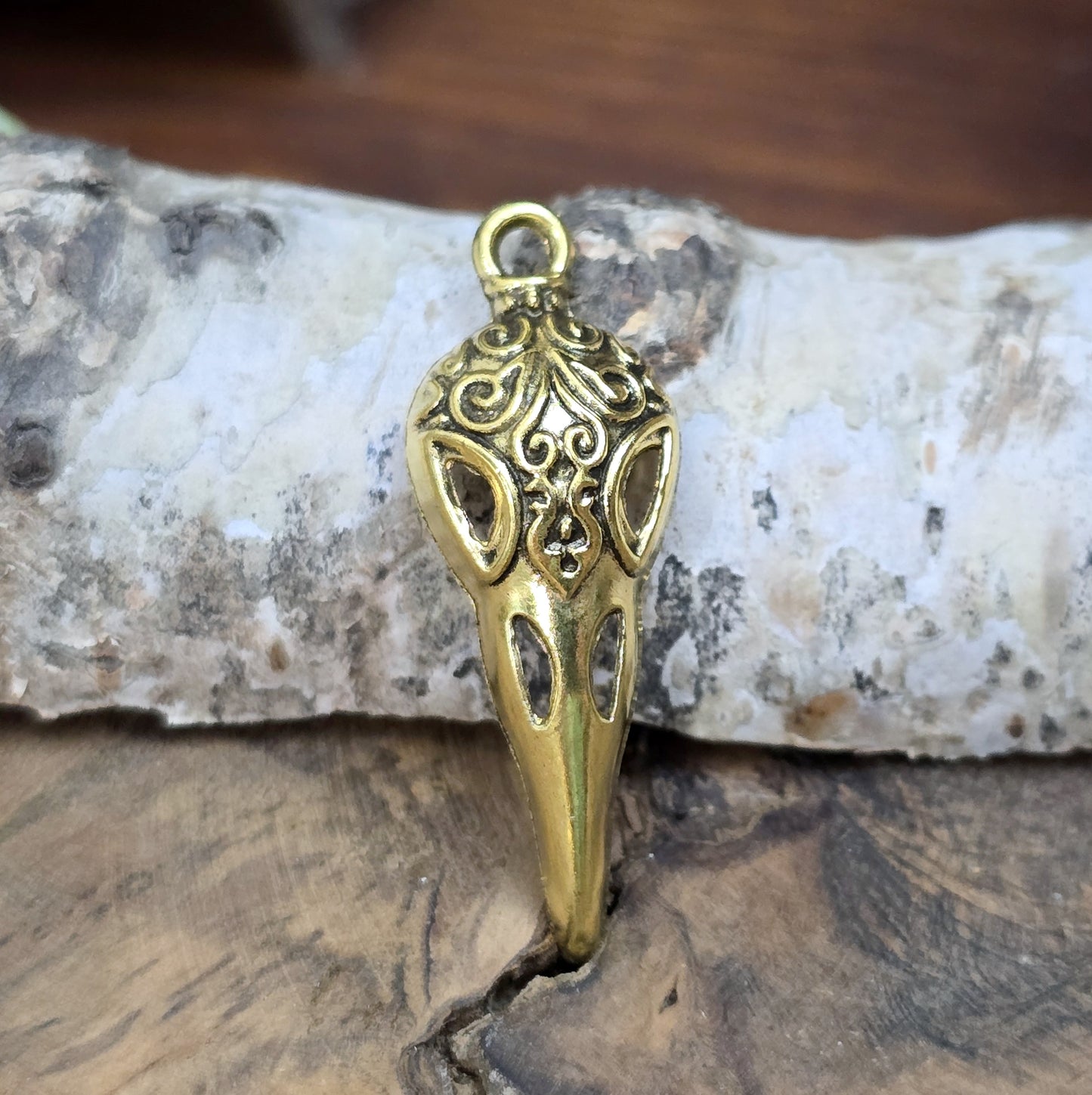 Das Bild zeigt einen detaillierten Krähenschädel mit Intarsien, gehalten in antik goldfarbenem Finish. Er ist einseitig geprägt und hat eine hohle Rückseite, was ihn leicht und vielseitig macht.
