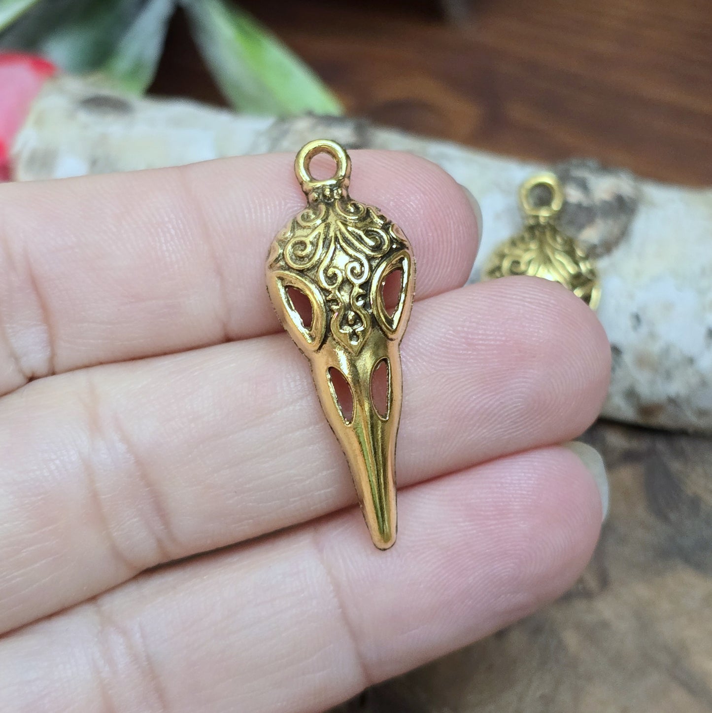 Das Bild zeigt einen detaillierten Krähenschädel mit Intarsien, gehalten in antik goldfarbenem Finish. Er ist einseitig geprägt und hat eine hohle Rückseite, was ihn leicht und vielseitig macht.
