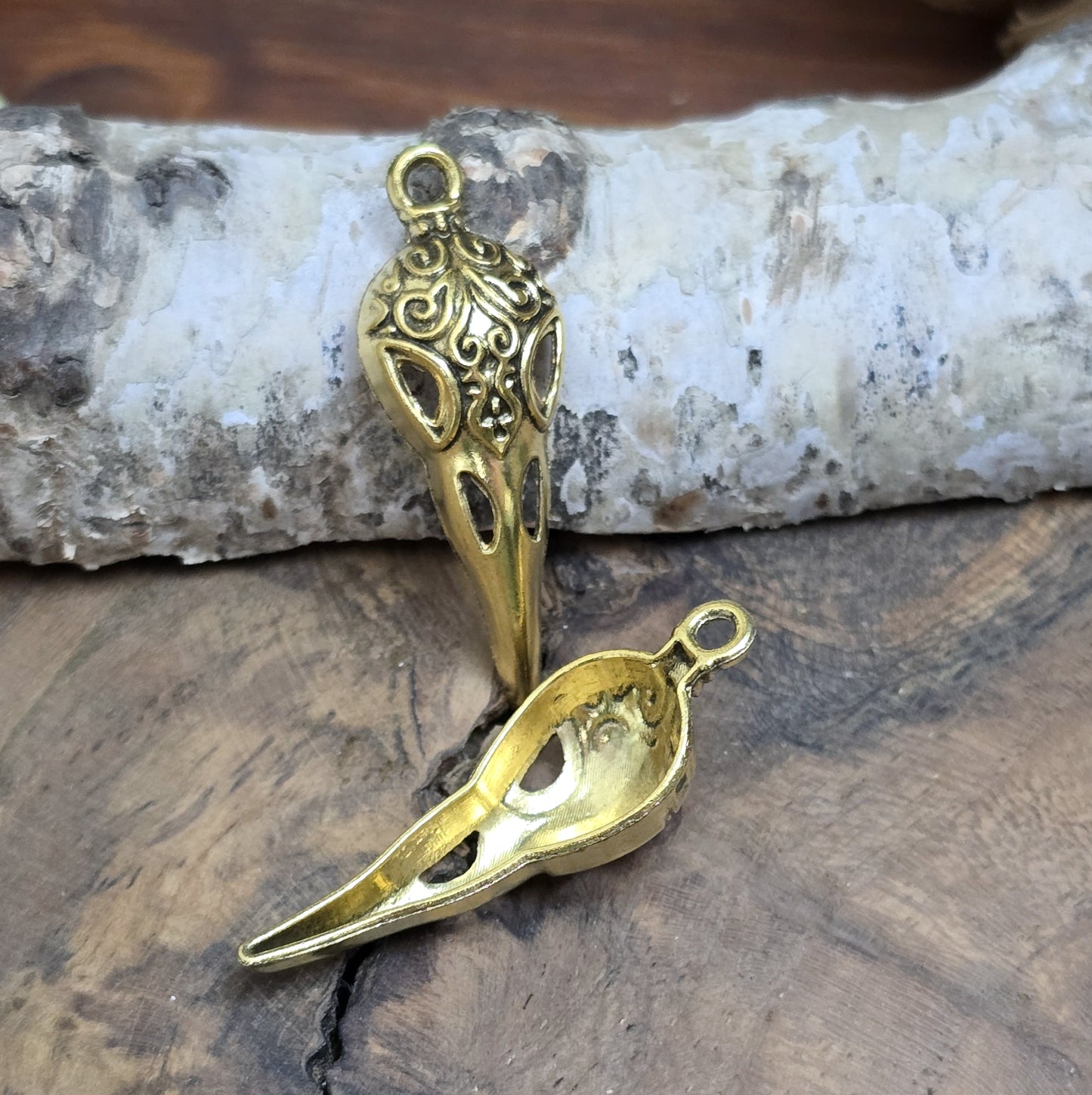 Das Bild zeigt einen detaillierten Krähenschädel mit Intarsien, gehalten in antik goldfarbenem Finish. Er ist einseitig geprägt und hat eine hohle Rückseite, was ihn leicht und vielseitig macht.