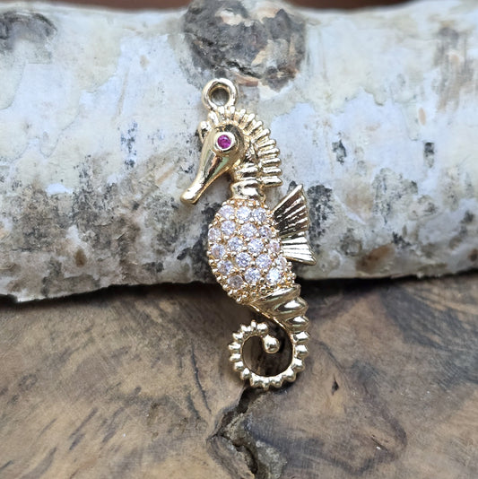 Das Bild zeigt einen eleganten Charms-Anhänger aus Messing, veredelt mit 24 Karat Vergoldung und funkelnden Strasssteinen. Das Seepferdchen, Symbol für Anmut und das Meer, wird hier in seiner ganzen Schönheit hervorgehoben.