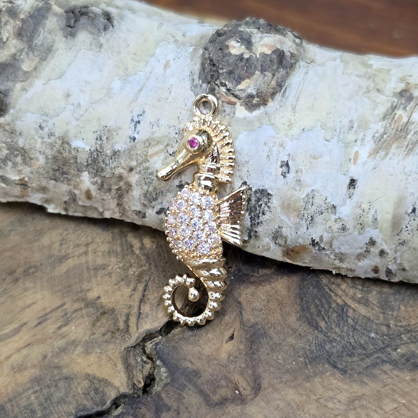 Das Bild zeigt einen eleganten Charms-Anhänger aus Messing, veredelt mit 24 Karat Vergoldung und funkelnden Strasssteinen. Das Seepferdchen, Symbol für Anmut und das Meer, wird hier in seiner ganzen Schönheit hervorgehoben.