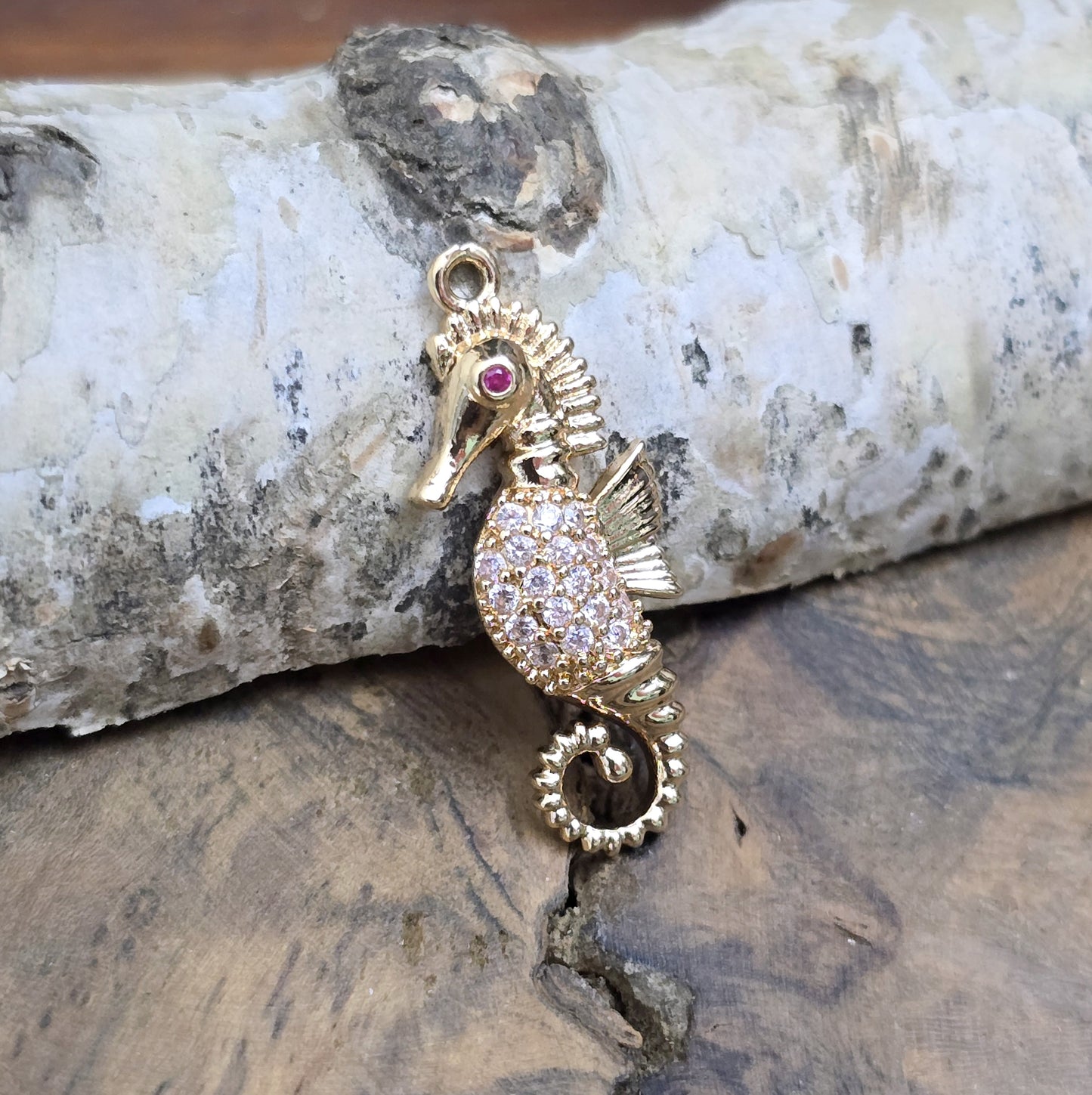 Das Bild zeigt einen eleganten Charms-Anhänger aus Messing, veredelt mit 24 Karat Vergoldung und funkelnden Strasssteinen. Das Seepferdchen, Symbol für Anmut und das Meer, wird hier in seiner ganzen Schönheit hervorgehoben.