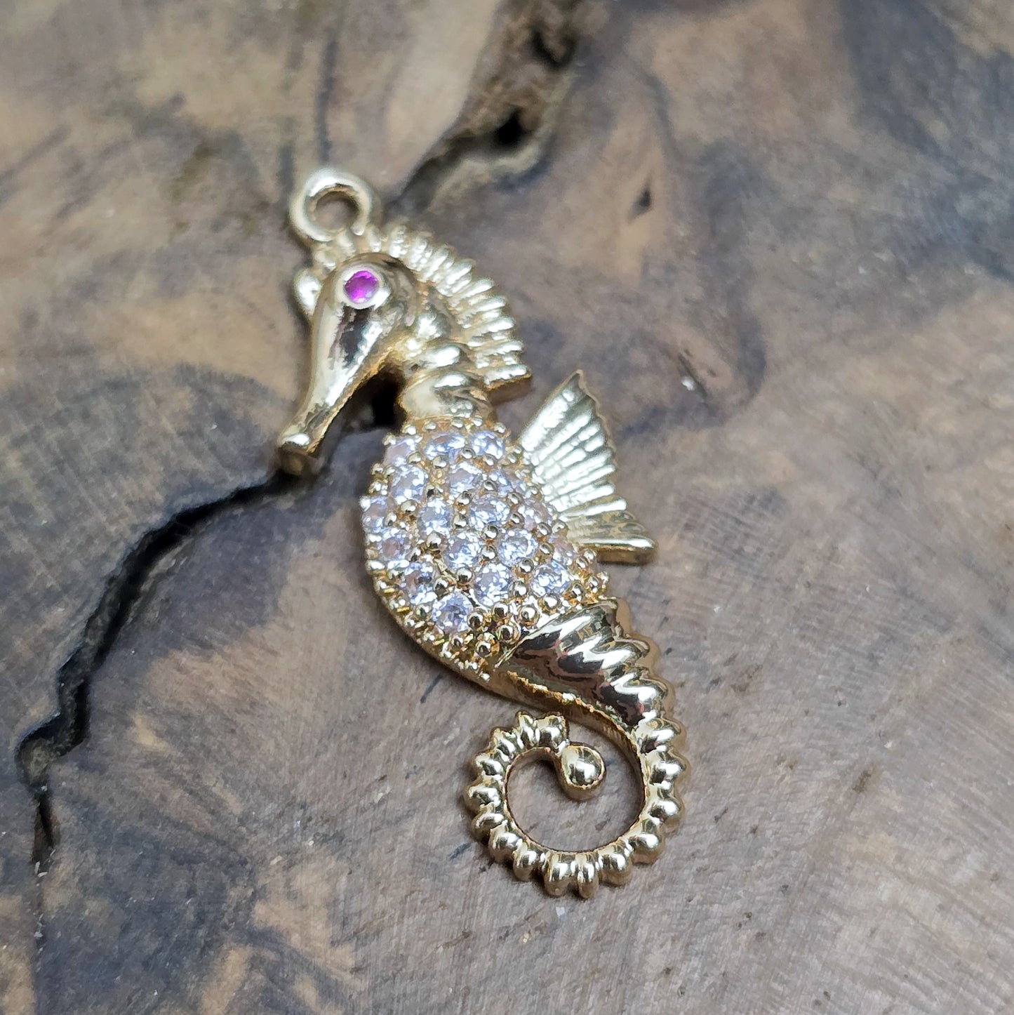 Das Bild zeigt einen eleganten Charms-Anhänger aus Messing, veredelt mit 24 Karat Vergoldung und funkelnden Strasssteinen. Das Seepferdchen, Symbol für Anmut und das Meer, wird hier in seiner ganzen Schönheit hervorgehoben.