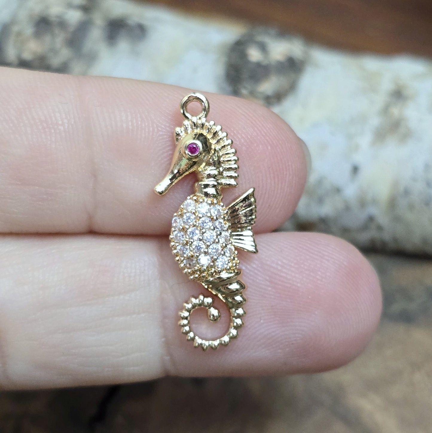 Das Bild zeigt einen eleganten Charms-Anhänger aus Messing, veredelt mit 24 Karat Vergoldung und funkelnden Strasssteinen. Das Seepferdchen, Symbol für Anmut und das Meer, wird hier in seiner ganzen Schönheit hervorgehoben.