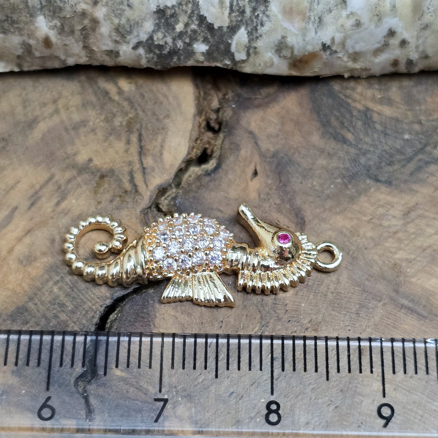 Das Bild zeigt einen eleganten Charms-Anhänger aus Messing, veredelt mit 24 Karat Vergoldung und funkelnden Strasssteinen. Das Seepferdchen, Symbol für Anmut und das Meer, wird hier in seiner ganzen Schönheit hervorgehoben.