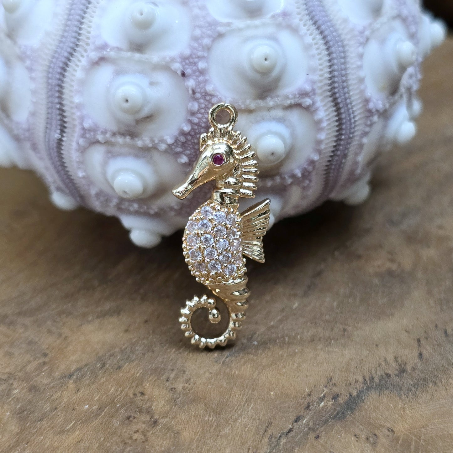 Das Bild zeigt einen eleganten Charms-Anhänger aus Messing, veredelt mit 24 Karat Vergoldung und funkelnden Strasssteinen. Das Seepferdchen, Symbol für Anmut und das Meer, wird hier in seiner ganzen Schönheit hervorgehoben.
