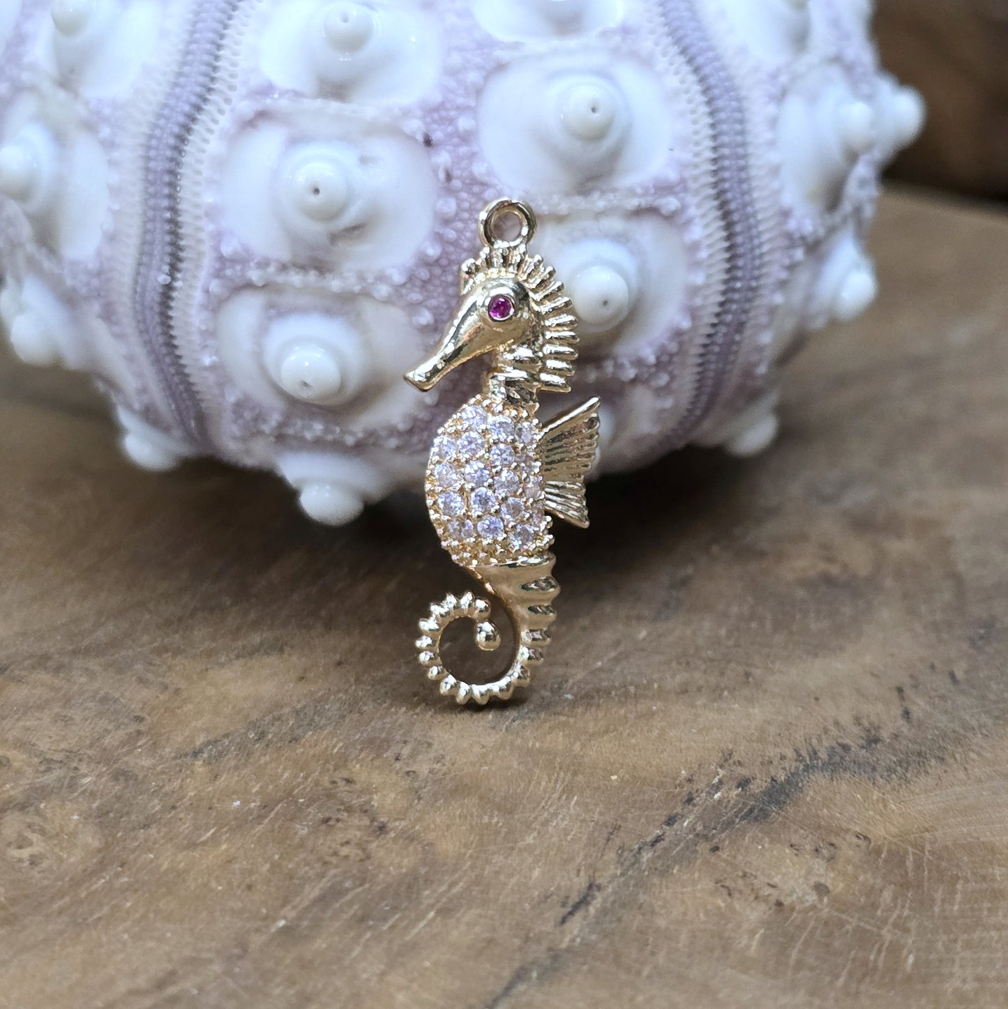 Das Bild zeigt einen eleganten Charms-Anhänger aus Messing, veredelt mit 24 Karat Vergoldung und funkelnden Strasssteinen. Das Seepferdchen, Symbol für Anmut und das Meer, wird hier in seiner ganzen Schönheit hervorgehoben.