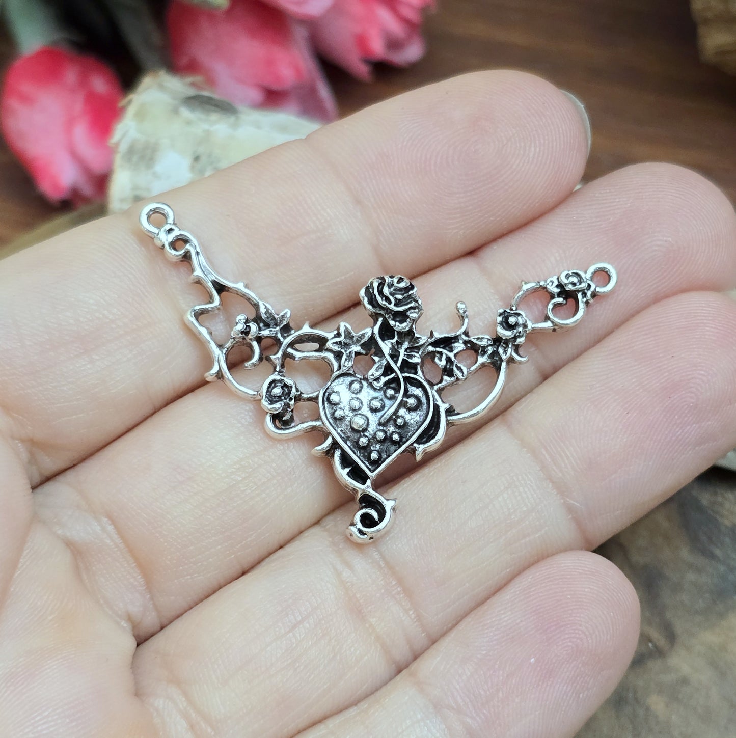 Das Bild zeigt eine Schmuckkomponente für Ketten, Choker und Armbänder. Der Verbinder ist antik silberfarbig und kann z.B. durch colorieren zu einem ganz persönlichen Schmuckteil werden. In der Mitte befindet sich ein Herz, umgeben von Rosen.