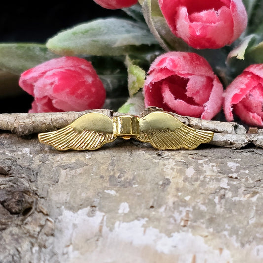 Auf dem Bild ist eine vergoldete Metallperle in Form von Engelsflügeln zu sehen. Mit einer Größe von 35 mm eignet sich diese Perle perfekt für die Gestaltung von Schutzengeln. Die Flügel sind kunstvoll verziert und glänzen in edlem Gold.