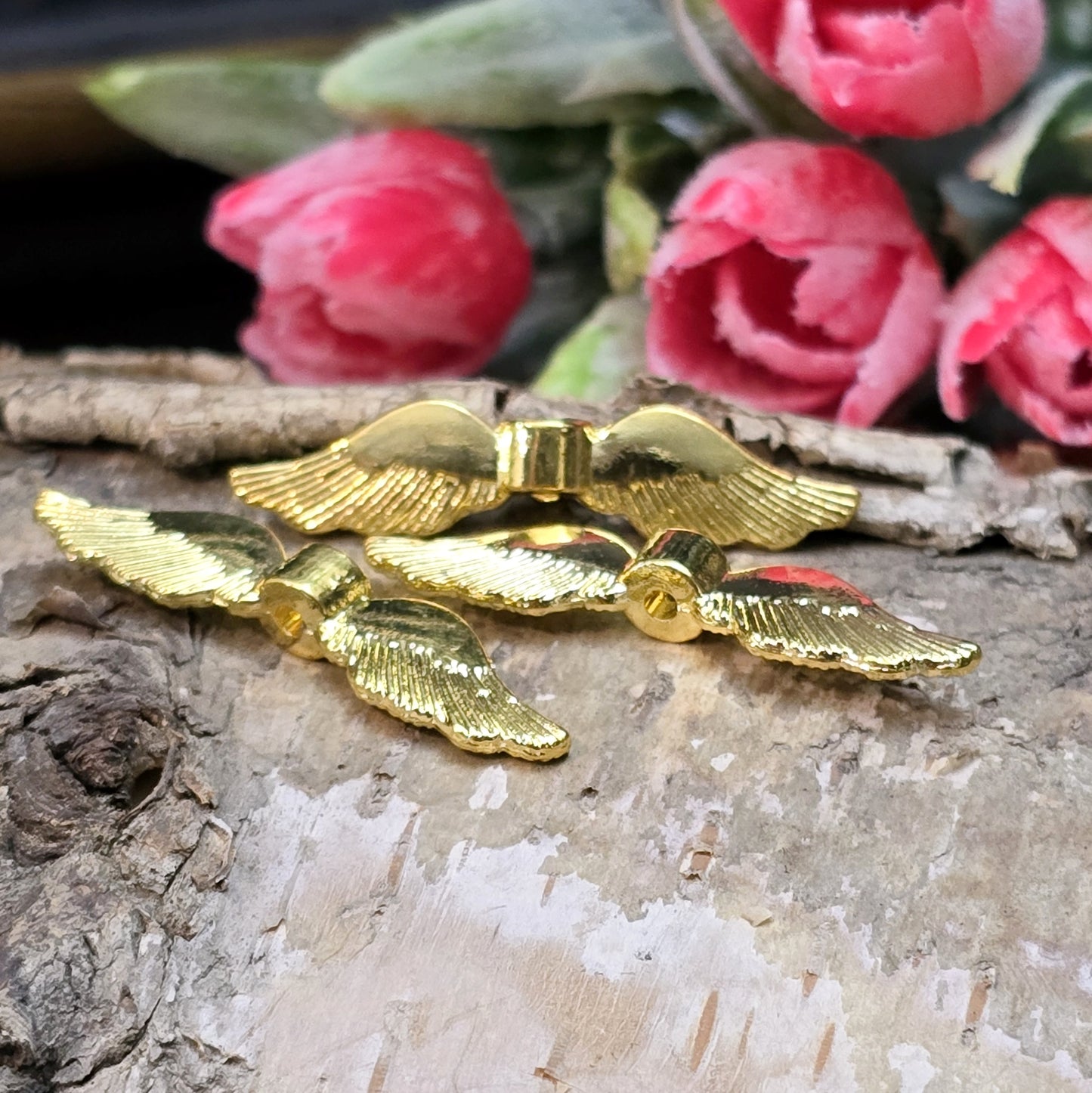 Auf dem Bild ist eine vergoldete Metallperle in Form von Engelsflügeln zu sehen. Mit einer Größe von 35 mm eignet sich diese Perle perfekt für die Gestaltung von Schutzengeln. Die Flügel sind kunstvoll verziert und glänzen in edlem Gold.