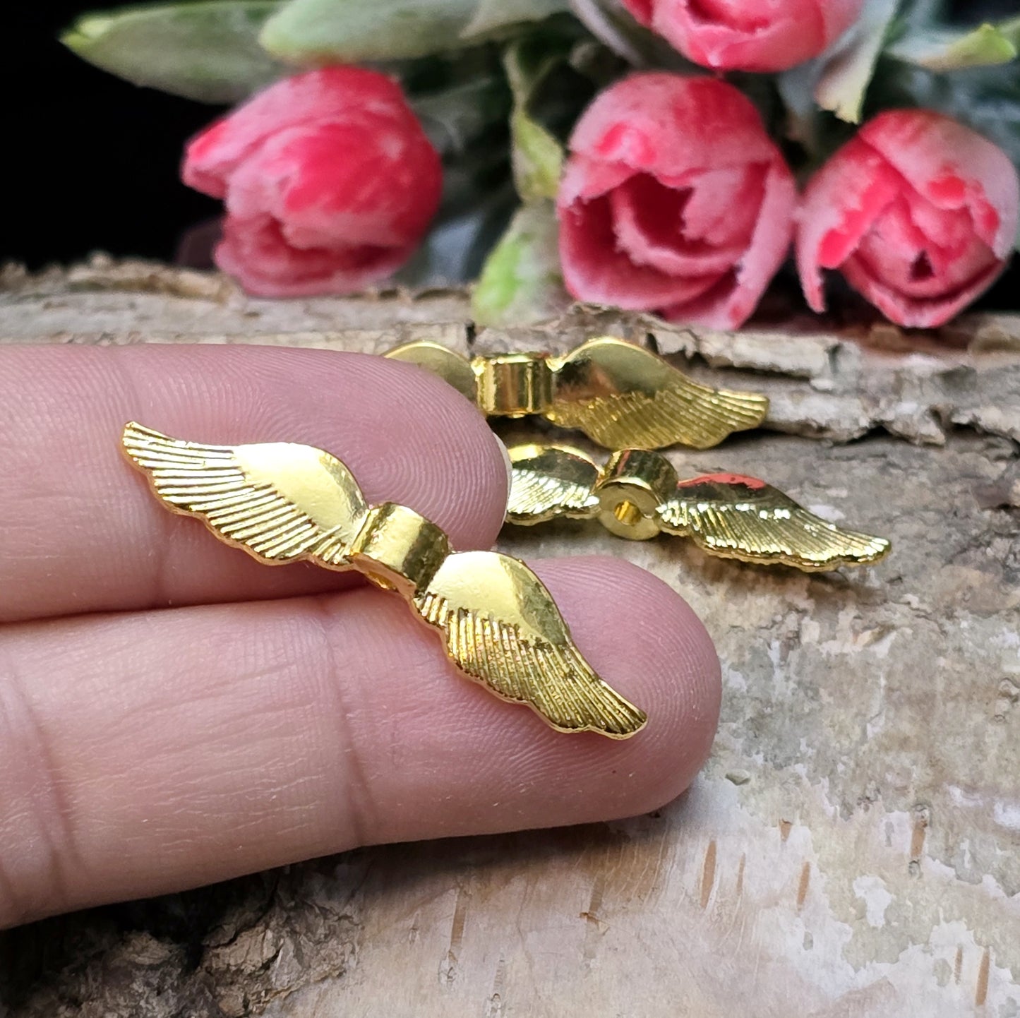Auf dem Bild ist eine vergoldete Metallperle in Form von Engelsflügeln zu sehen. Mit einer Größe von 35 mm eignet sich diese Perle perfekt für die Gestaltung von Schutzengeln. Die Flügel sind kunstvoll verziert und glänzen in edlem Gold.
