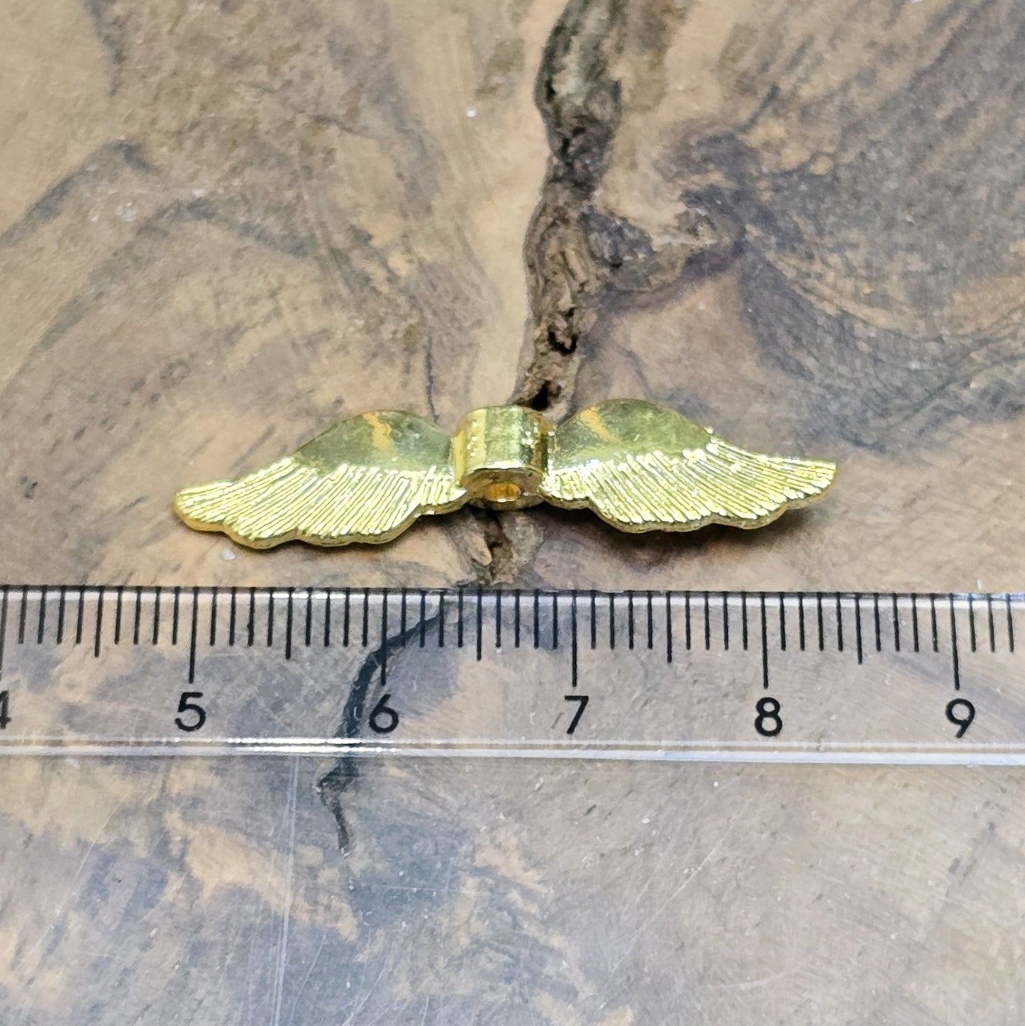 Auf dem Bild ist eine vergoldete Metallperle in Form von Engelsflügeln zu sehen. Mit einer Größe von 35 mm eignet sich diese Perle perfekt für die Gestaltung von Schutzengeln. Die Flügel sind kunstvoll verziert und glänzen in edlem Gold.