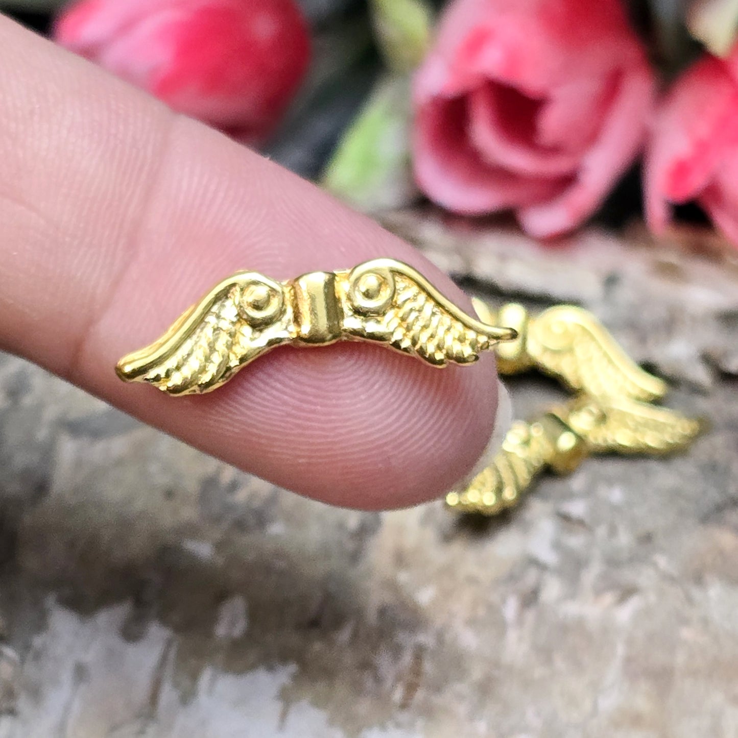 Auf dem Bild sind vergoldete Metallperlen in Form von Engelsflügeln zu sehen. Mit einer Größe von 22 mm eignen sie sich ideal für die Herstellung von Schmuckstücken wie Schutzengeln und anderen kreativen DIY-Projekten.