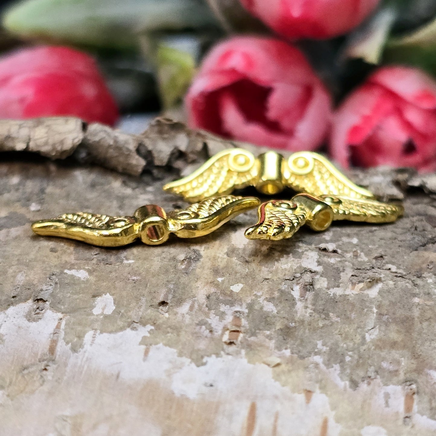 Auf dem Bild sind vergoldete Metallperlen in Form von Engelsflügeln zu sehen. Mit einer Größe von 22 mm eignen sie sich ideal für die Herstellung von Schmuckstücken wie Schutzengeln und anderen kreativen DIY-Projekten.