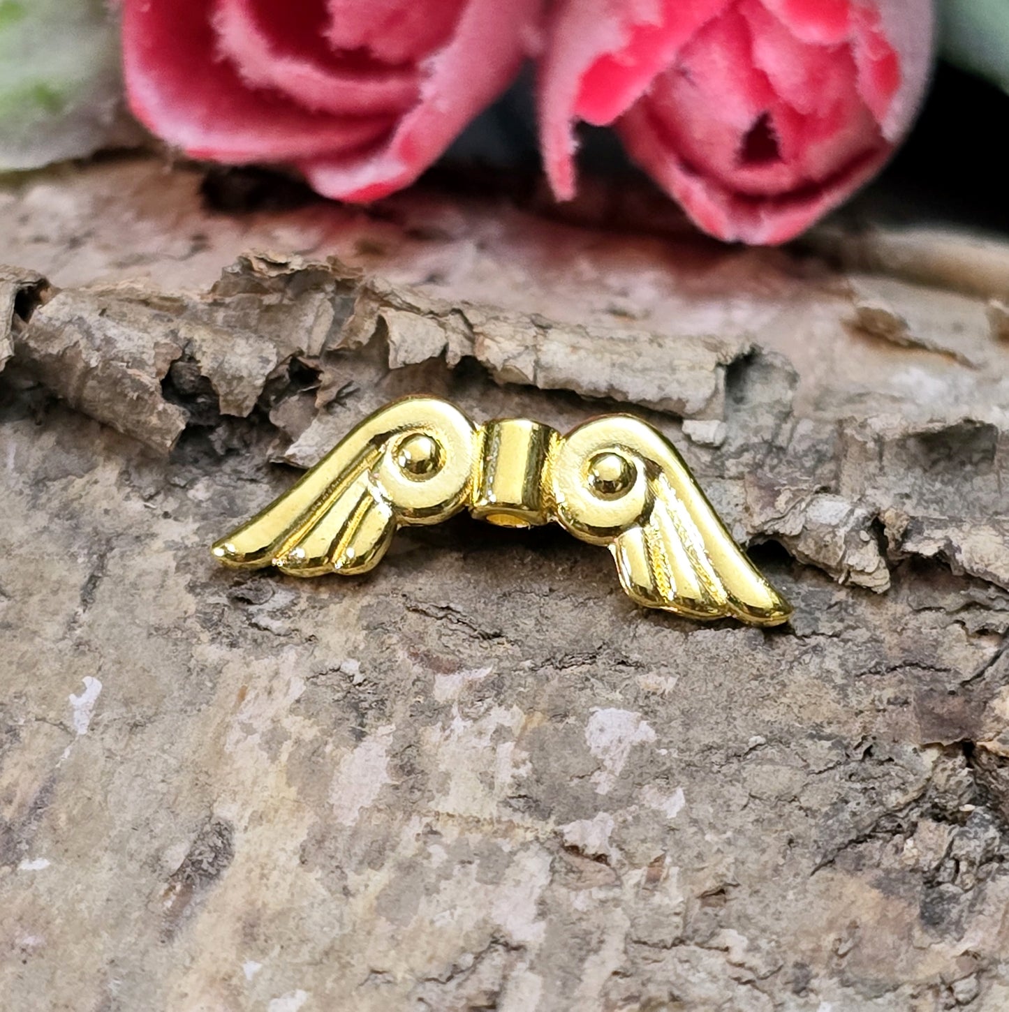 Das Bild zeigt vergoldete Metallperlen in Form von Engelsflügeln. Die Perlen sind 22 mm lang und zeichnen sich durch zarte, filigrane Details aus, die den Flügeln eine elegante und anmutige Erscheinung verleihen.