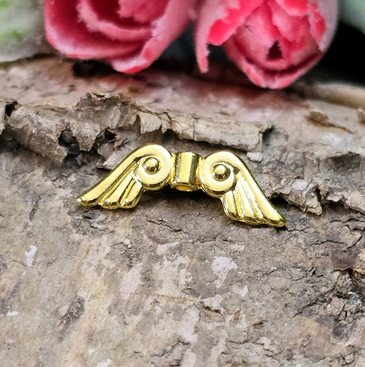 Das Bild zeigt vergoldete Metallperlen in Form von Engelsflügeln. Die Perlen sind 22 mm lang und zeichnen sich durch zarte, filigrane Details aus, die den Flügeln eine elegante und anmutige Erscheinung verleihen.