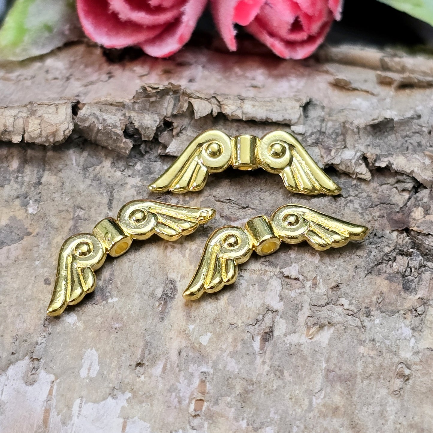 Das Bild zeigt vergoldete Metallperlen in Form von Engelsflügeln. Die Perlen sind 22 mm lang und zeichnen sich durch zarte, filigrane Details aus, die den Flügeln eine elegante und anmutige Erscheinung verleihen.