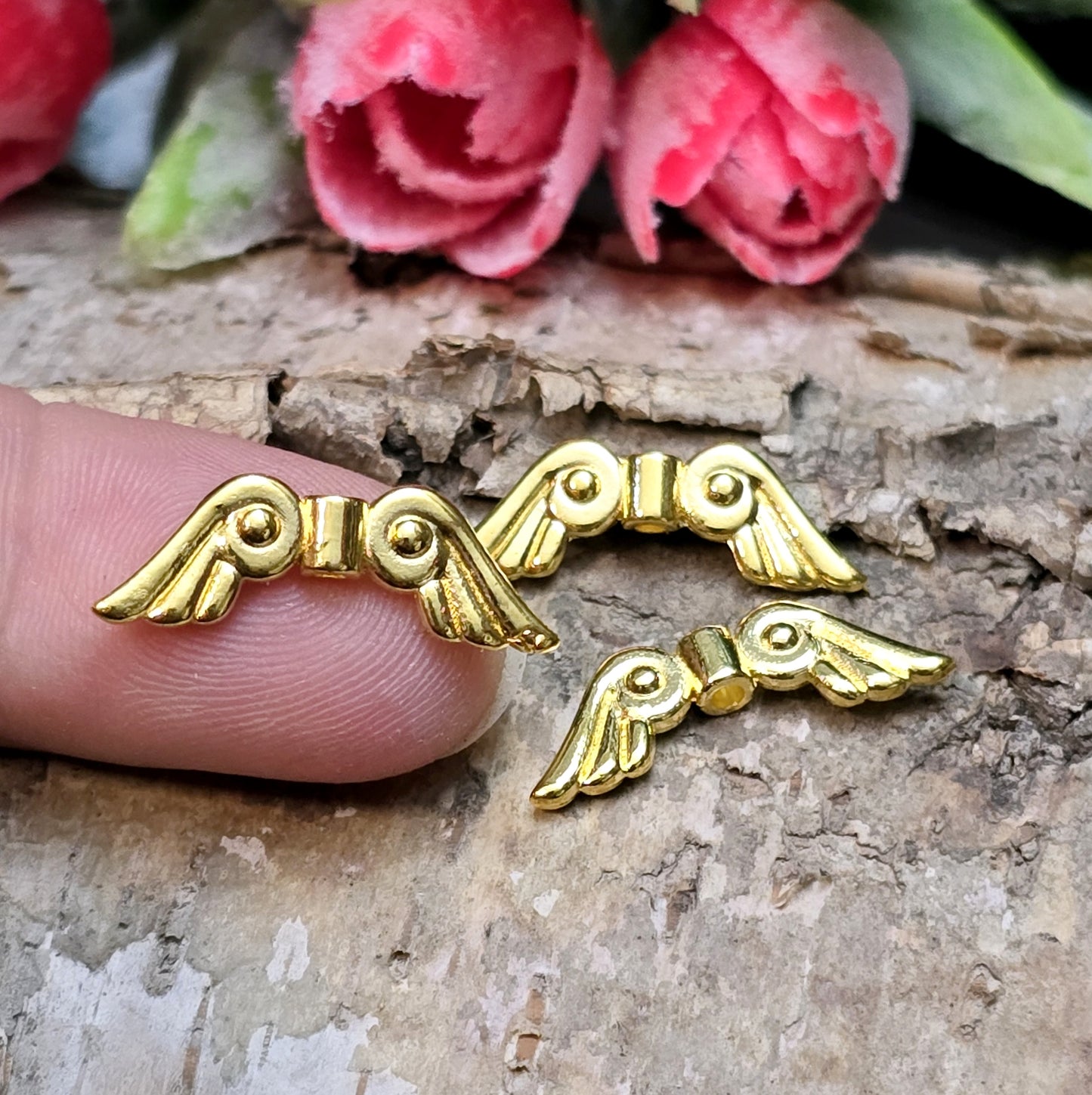 Das Bild zeigt vergoldete Metallperlen in Form von Engelsflügeln. Die Perlen sind 22 mm lang und zeichnen sich durch zarte, filigrane Details aus, die den Flügeln eine elegante und anmutige Erscheinung verleihen.