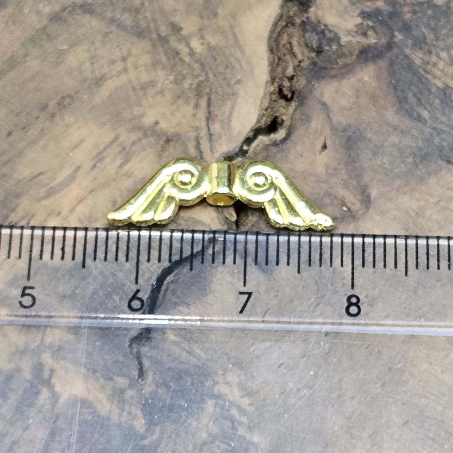 Das Bild zeigt vergoldete Metallperlen in Form von Engelsflügeln. Die Perlen sind 22 mm lang und zeichnen sich durch zarte, filigrane Details aus, die den Flügeln eine elegante und anmutige Erscheinung verleihen.