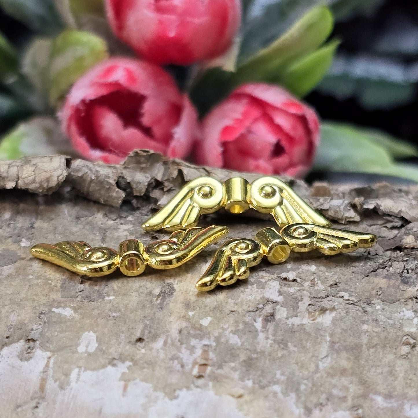 Das Bild zeigt vergoldete Metallperlen in Form von Engelsflügeln. Die Perlen sind 22 mm lang und zeichnen sich durch zarte, filigrane Details aus, die den Flügeln eine elegante und anmutige Erscheinung verleihen.