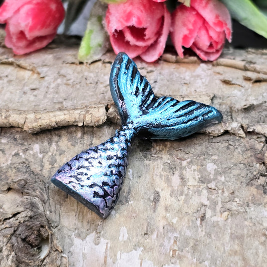 Das Bild zeigt eine handgefertigte Schwanzflosse einer Meerjungfrau aus Kunstharz. Die Flosse ist detailliert bemalt in sanften Farben und hat eine flache Rückseite. Sie eignet sich ideal als Cabochon für Schmuck oder als Dekoration für Bastelprojekte.