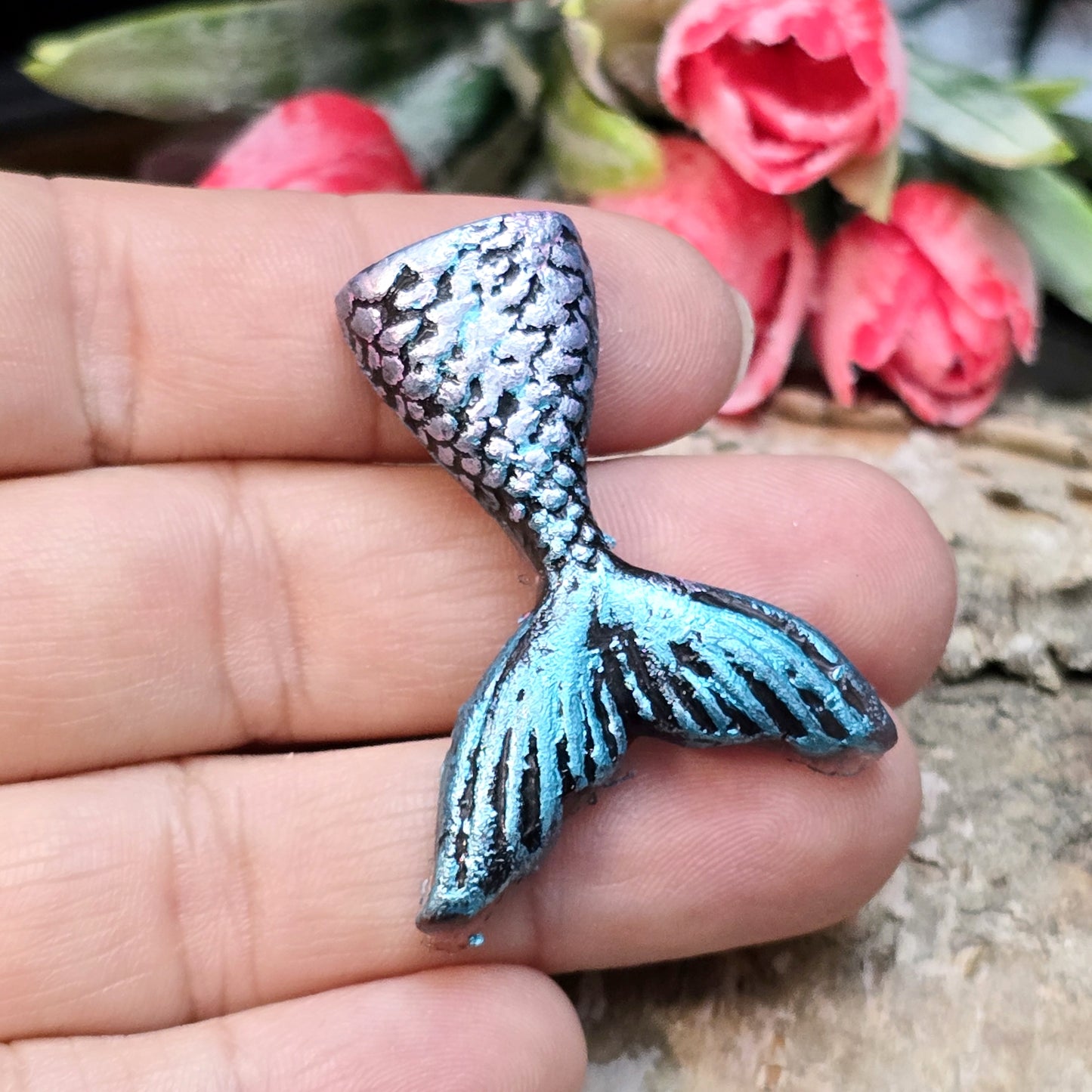 Das Bild zeigt eine handgefertigte Schwanzflosse einer Meerjungfrau aus Kunstharz. Die Flosse ist detailliert bemalt in sanften Farben und hat eine flache Rückseite. Sie eignet sich ideal als Cabochon für Schmuck oder als Dekoration für Bastelprojekte.