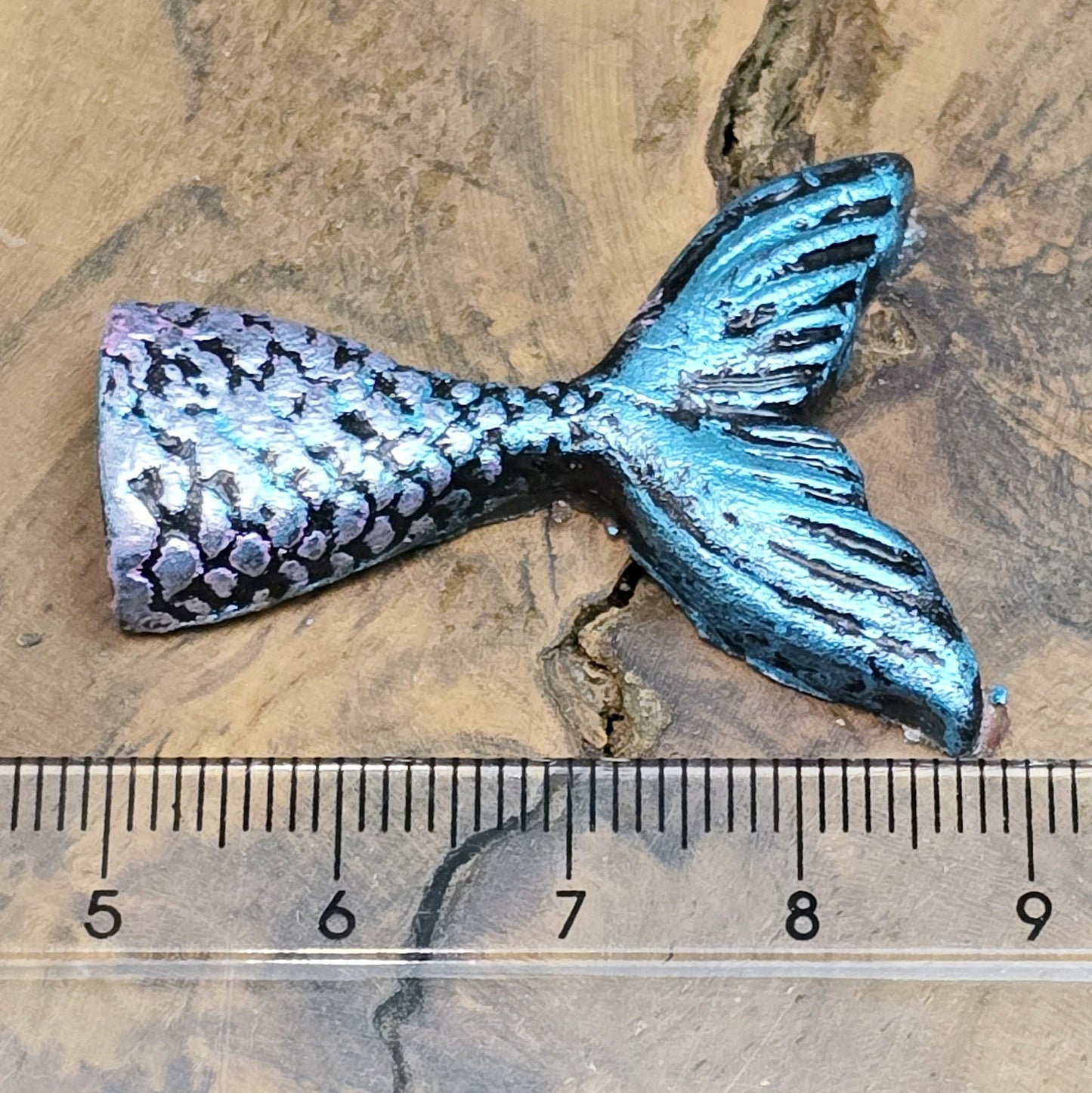 Das Bild zeigt eine handgefertigte Schwanzflosse einer Meerjungfrau aus Kunstharz. Die Flosse ist detailliert bemalt in sanften Farben und hat eine flache Rückseite. Sie eignet sich ideal als Cabochon für Schmuck oder als Dekoration für Bastelprojekte.