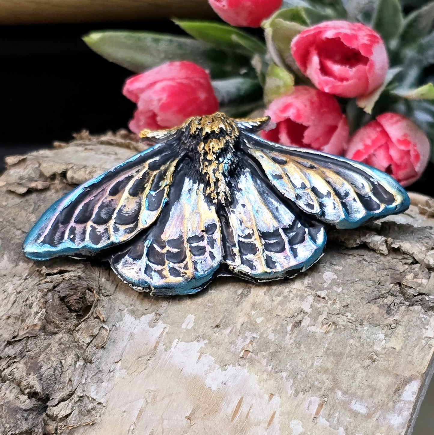 Auf dem Bild ist ein handgefertigter Cabochon in Form einer Deathmoth-Motte zu sehen. Das detailreiche Kunstharzstück zeigt die ausgebreiteten Flügel der mystischen Motte, verziert mit feinen Mustern und Schattierungen. Die Farbgebung betont die Struktur, wodurch das Motiv lebendig wirkt. Die Rückseite ist flach, sodass es sich gut für Schmuck oder Bastelarbeiten eignet. Die Motte liegt auf einem dunklen Untergrund, was ihren geheimnisvollen Charakter unterstreicht.
