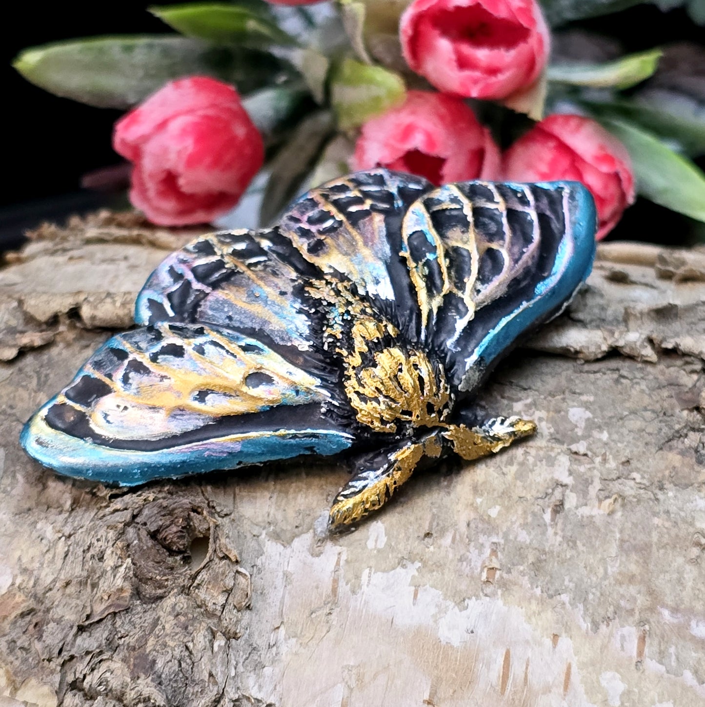 Auf dem Bild ist ein handgefertigter Cabochon in Form einer Deathmoth-Motte zu sehen. Das detailreiche Kunstharzstück zeigt die ausgebreiteten Flügel der mystischen Motte, verziert mit feinen Mustern und Schattierungen. Die Farbgebung betont die Struktur, wodurch das Motiv lebendig wirkt. Die Rückseite ist flach, sodass es sich gut für Schmuck oder Bastelarbeiten eignet. Die Motte liegt auf einem dunklen Untergrund, was ihren geheimnisvollen Charakter unterstreicht.