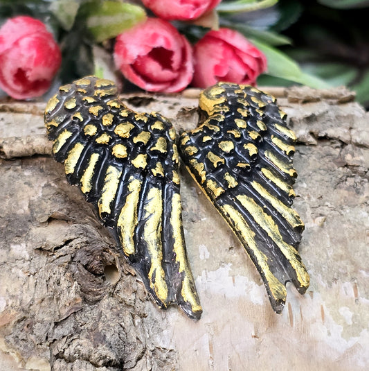 Auf dem Bild sind zwei handgefertigte Engelsflügel aus Kunstharz zu sehen. Die Flügel sind mit feinen, handbemalten Details verziert und haben eine flache Rückseite, die ideal für Schmuckherstellung oder Bastelprojekte geeignet ist.