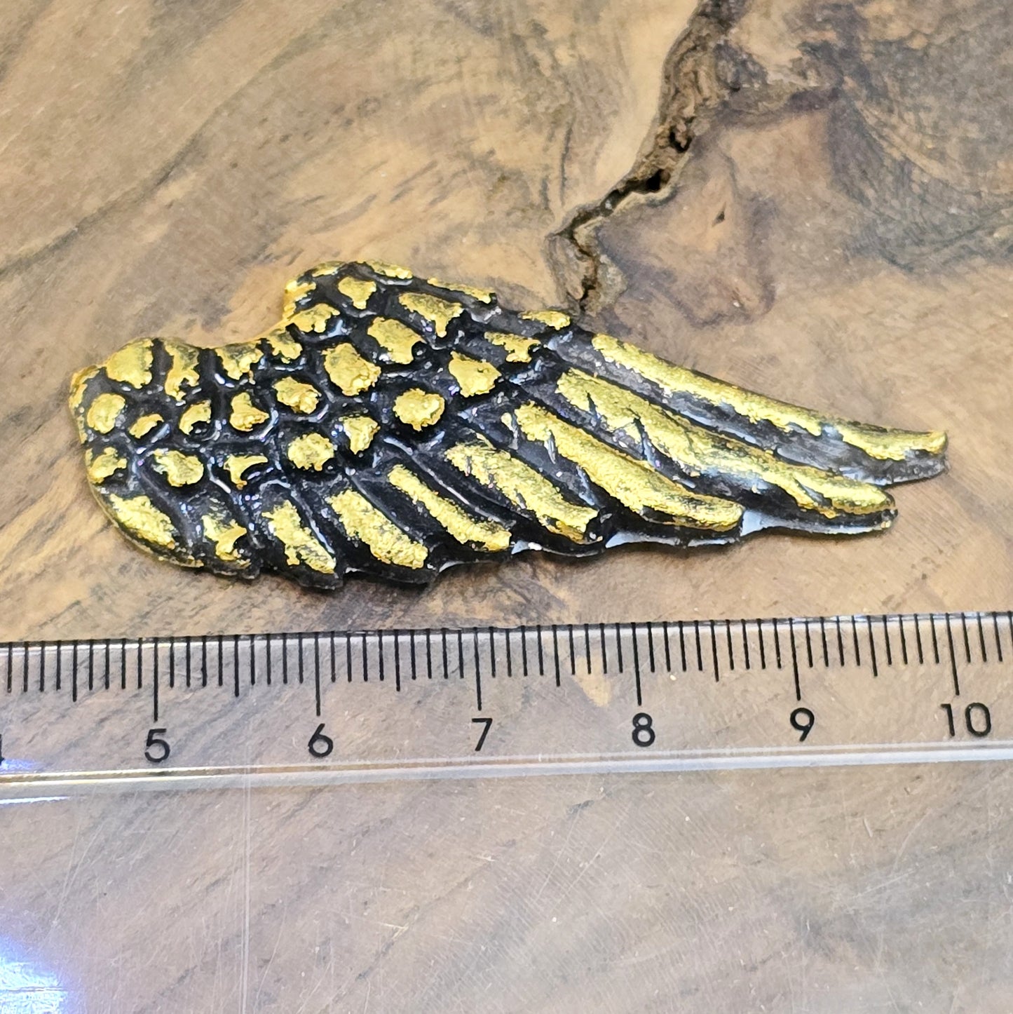 Auf dem Bild sind zwei handgefertigte Engelsflügel aus Kunstharz zu sehen. Die Flügel sind mit feinen, handbemalten Details verziert und haben eine flache Rückseite, die ideal für Schmuckherstellung oder Bastelprojekte geeignet ist.